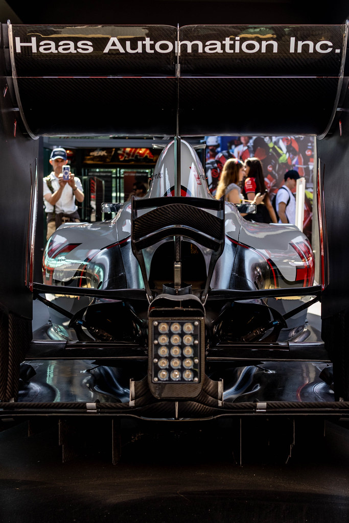 The rear wing and back of a Haas Formula 1 car on display, people taking photos behind it