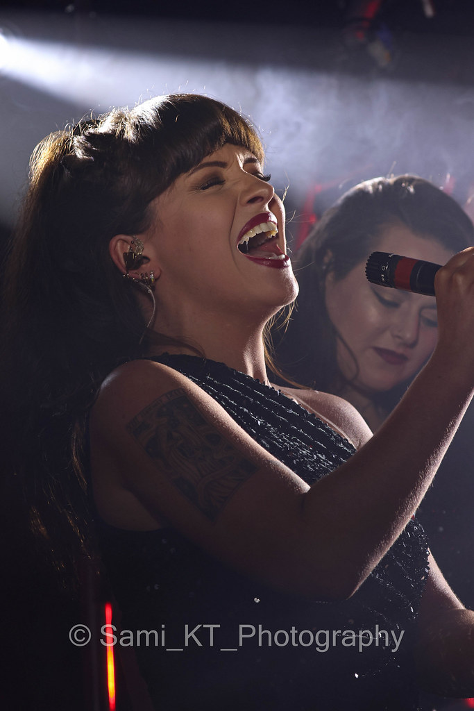 A singer on stage, eyes closed mid-song, lit by a beam of light